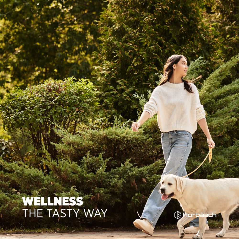 Woman walking a golden retriever outdoors while holding Iron + Vitamin C Gummies.