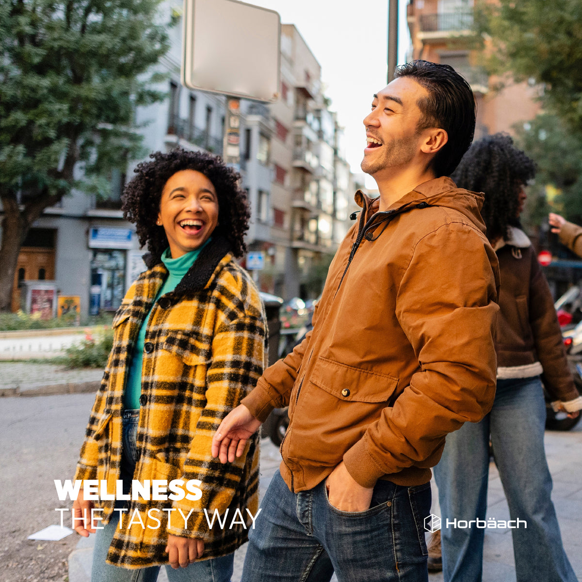 Young adults laughing and walking on a city street, with the text 'WELLNESS THE TASTY WAY' and Horbäach logo visible.