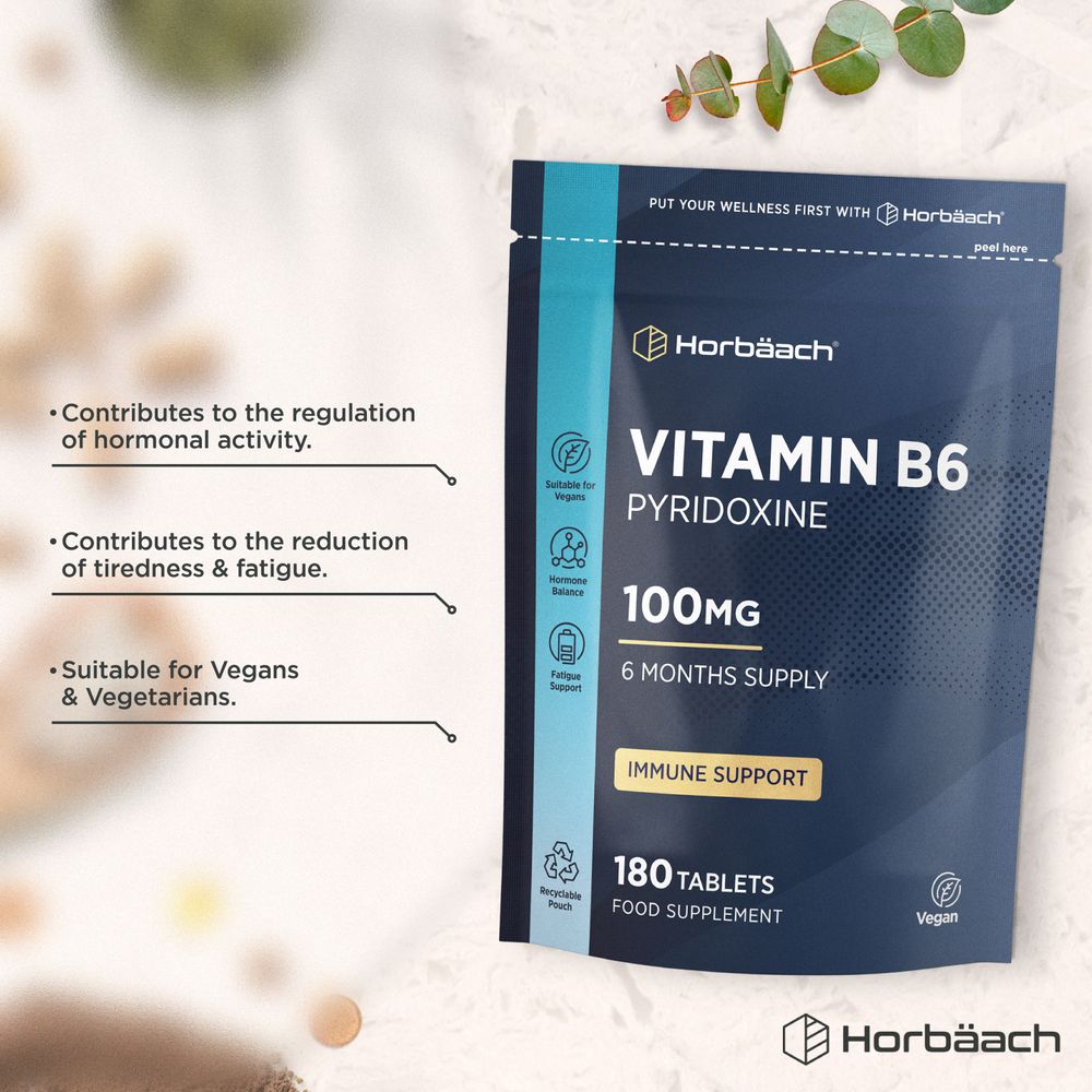 A hand holds a Vitamin B6 100mg tablet, showing its size and scale.