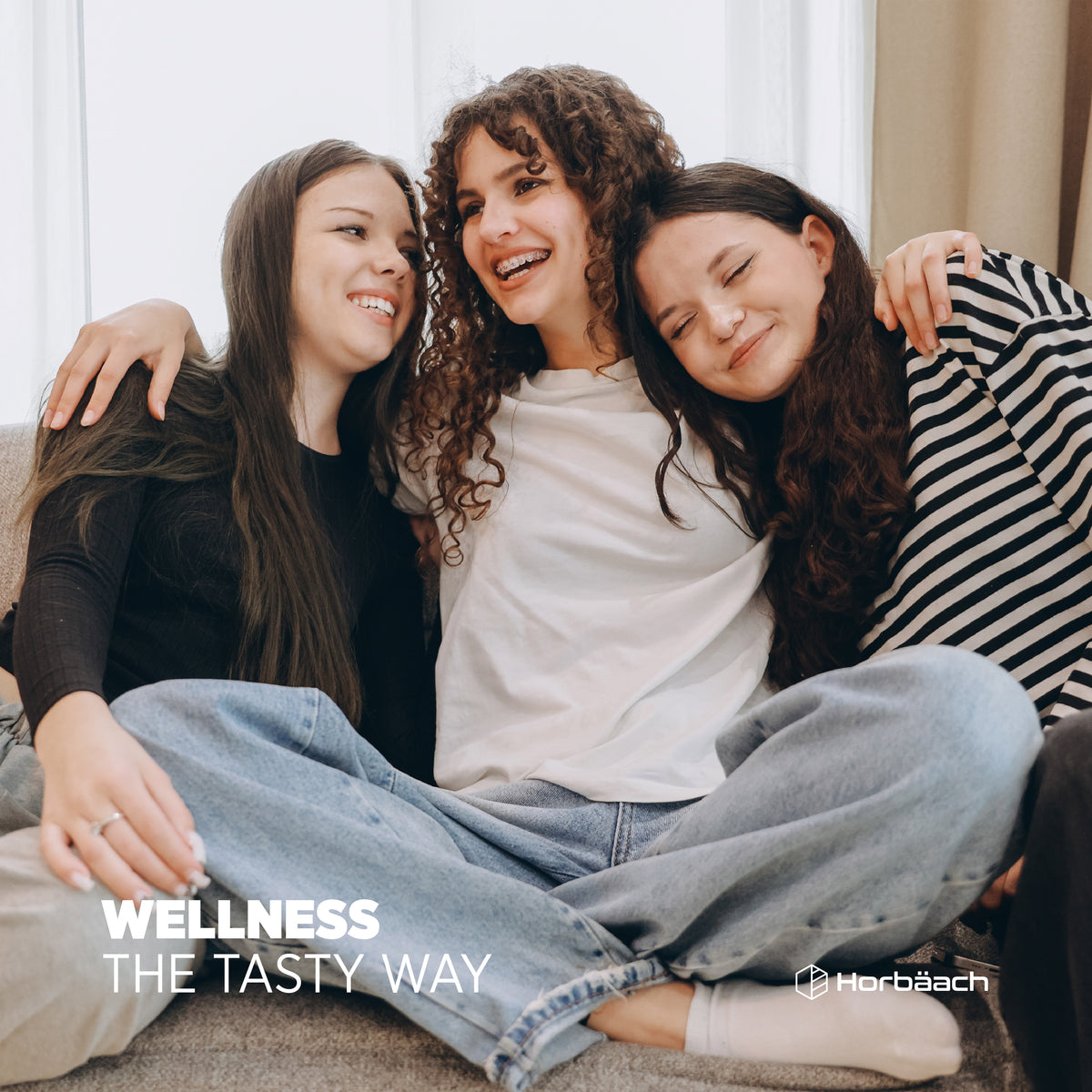 Three young women smiling and hugging on a couch. Text reads 'WELLNESS THE TASTY WAY' with 'Horbäach' logo visible.