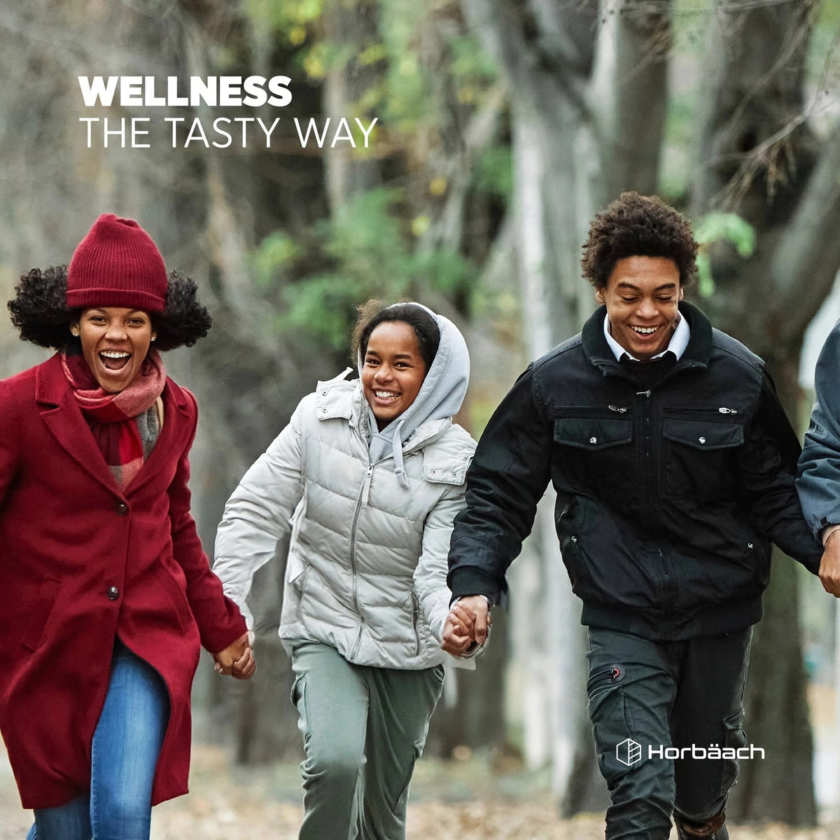 Three young adults in winter clothing run and laugh outdoors, enjoying each other's company while holding hands.